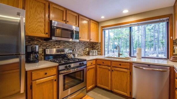 Una cocina moderna con armarios de madera, electrodomésticos de acero inoxidable y un amplio ventanal con vistas a árboles.