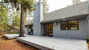 Una casa moderna con terraza de madera, una chimenea y ventanas amplias.