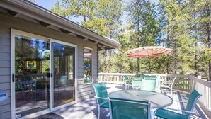 A covered deck with a table and chairs, a sliding glass door, and an umbrella. - Sparks 7 (Bend)