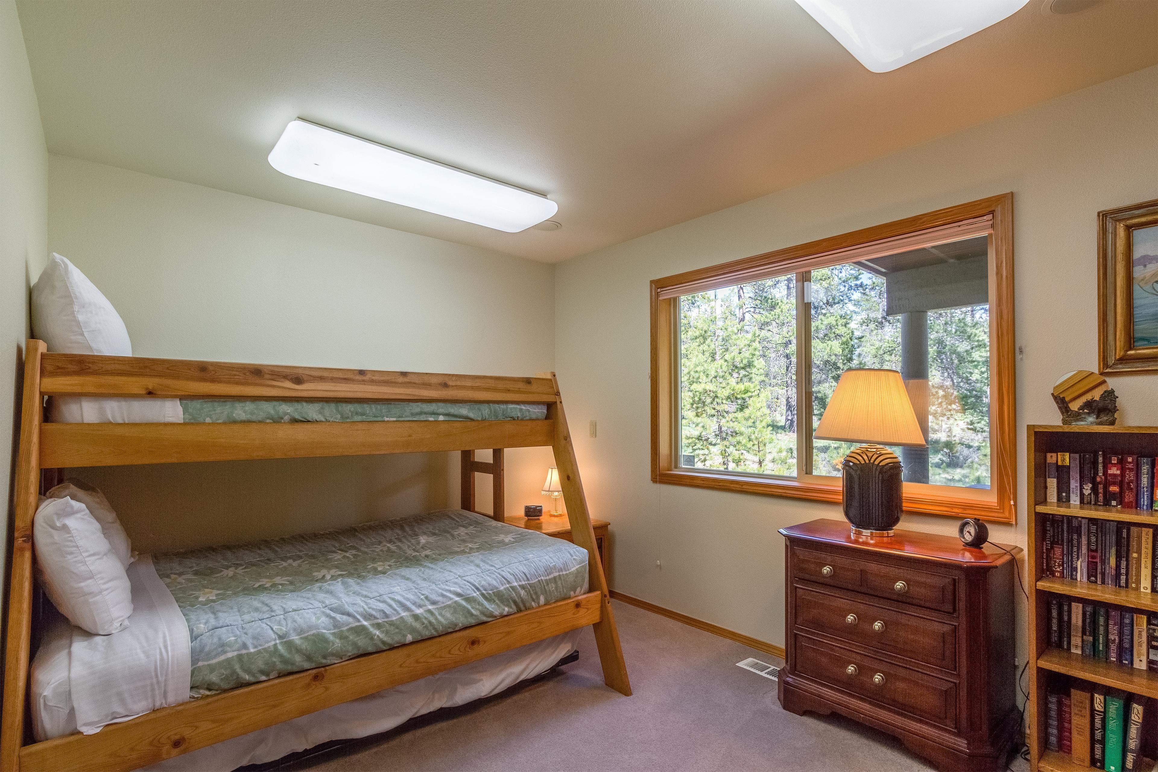A bunk bed with a bedside lamp and a wooden dresser with a lamp.