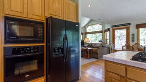 A kitchen with wooden cabinets, a black refrigerator, a microwave, and an oven. There is a dining area with a table and chairs, and a sign that reads "The Nepute Family". - Sparks 7 (Bend)