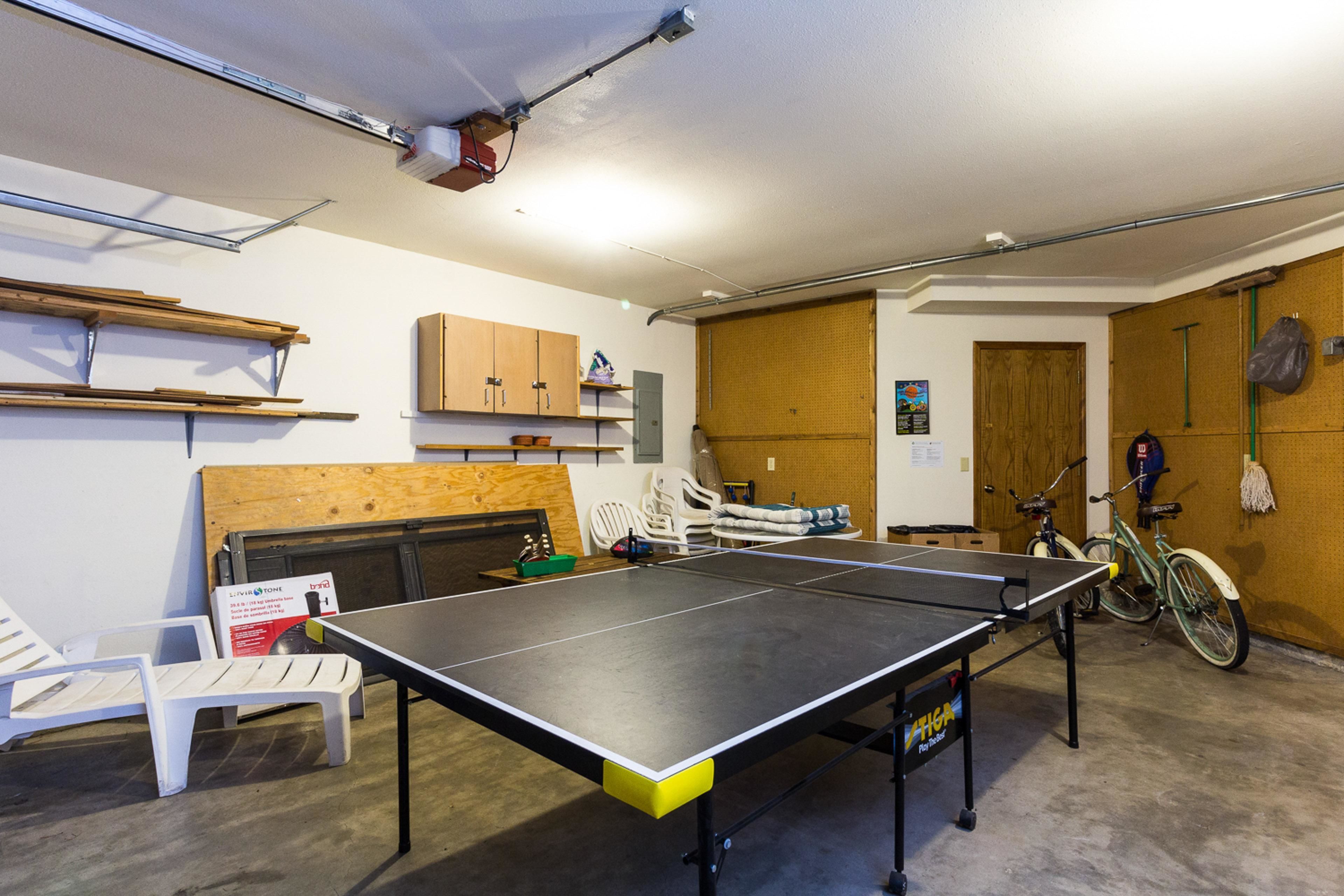 A room with a ping pong table, a bicycle, and a bed.