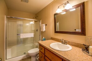 A bathroom with a glass-enclosed shower, a white sink, and a wooden vanity. - Grizzly 2 (Bend)