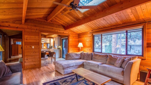 A cozy log cabin interior with a large sectional sofa, a wooden coffee table, and a dining area visible through an open doorway. - Grizzly 5 (Bend)