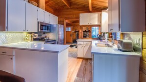 A modern kitchen with white cabinetry, a central island, and a wooden ceiling. - Grizzly 5 (Bend)