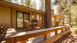 A wooden deck with a picnic table and chairs, a grill, and a stack of firewood. - Grizzly 5 (Bend)