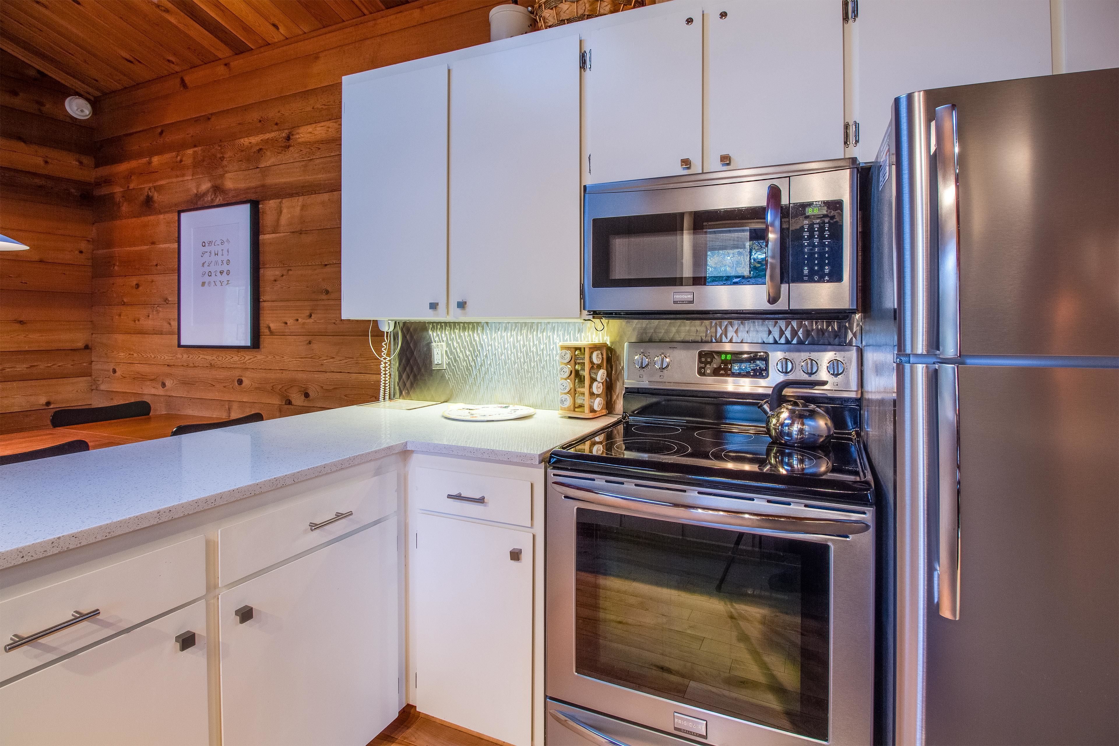 Una cocina moderna con electrodomésticos de acero inoxidable, armarios blancos y techo de madera.