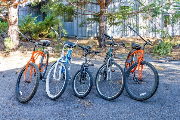 Quatro bicicletas estacionadas em fila sobre pavimento, com árvores e um edifício ao fundo.