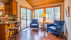 A modern kitchen with wooden cabinets, a bar area with stools, and large windows offering a view of the outdoors. - Hoodoo 3 (Bend)