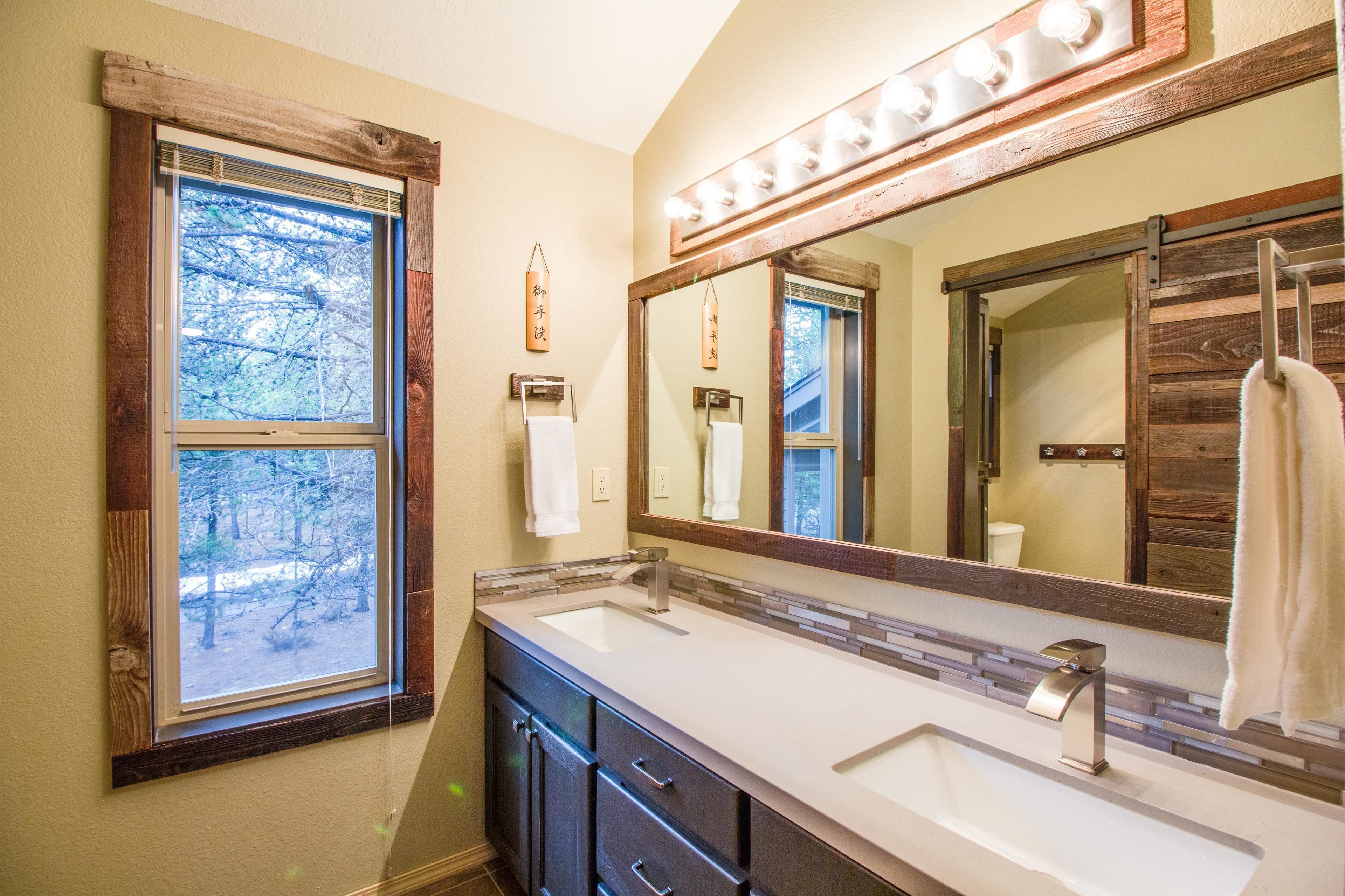 A bathroom with a large mirror, vanity with a sink, and a window with a view of trees.