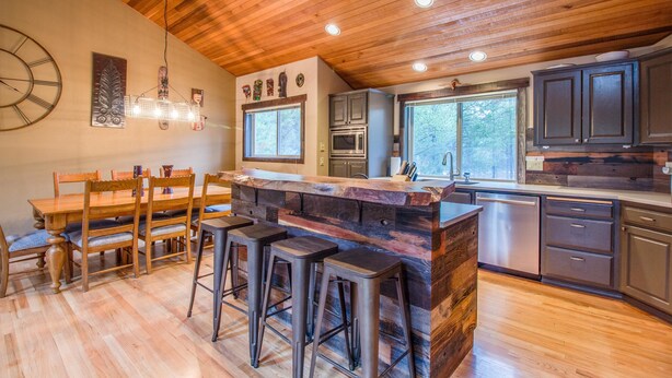 A kitchen with wooden ceiling, bar stools, a dining table, and a large window. - Hoodoo 5 (Bend)