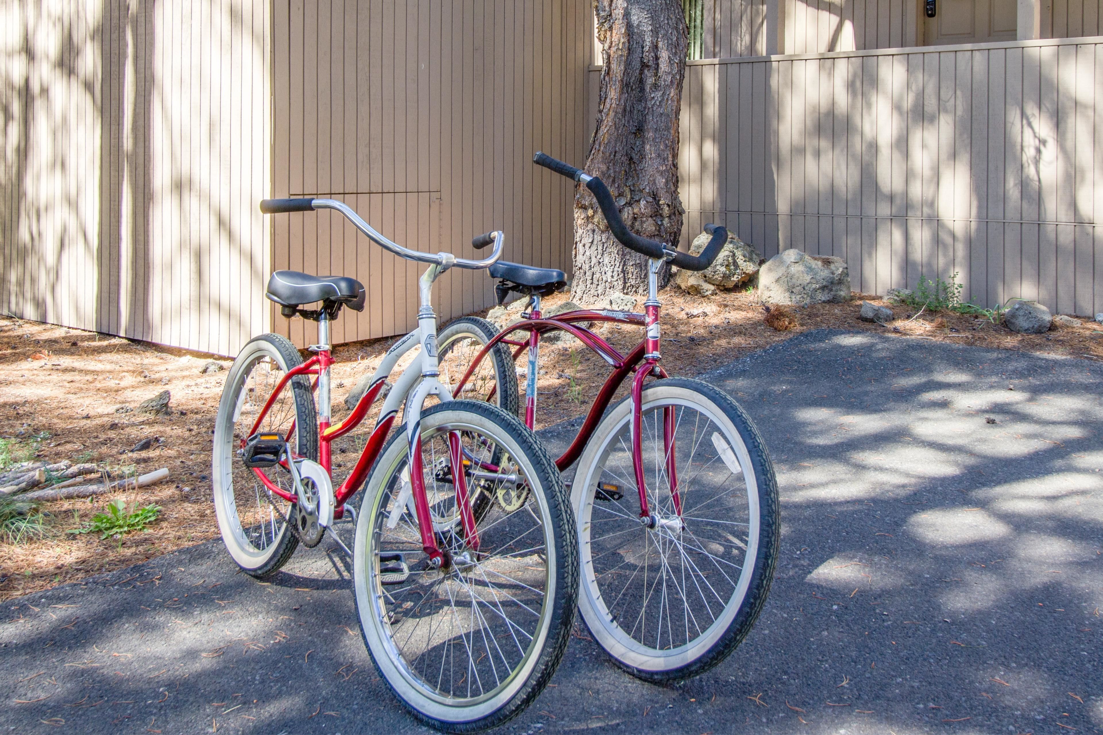 Two bicycles parked next to a tree and a building.