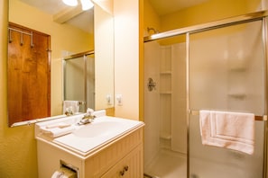 Un baño con lavamanos blanco, espejo y cabina de ducha con paredes de vidrio.