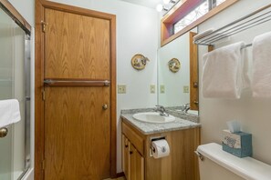 A bathroom with a wooden door, a sink with a mirror, and a toilet with a tissue box. - Juniper 9 (Bend)