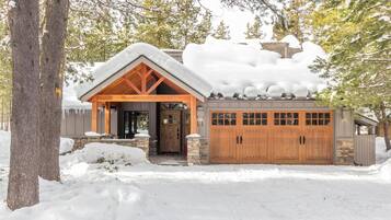 Une cabane avec des fondations en pierre, des portes de garage en bois et un toit recouvert de neige.