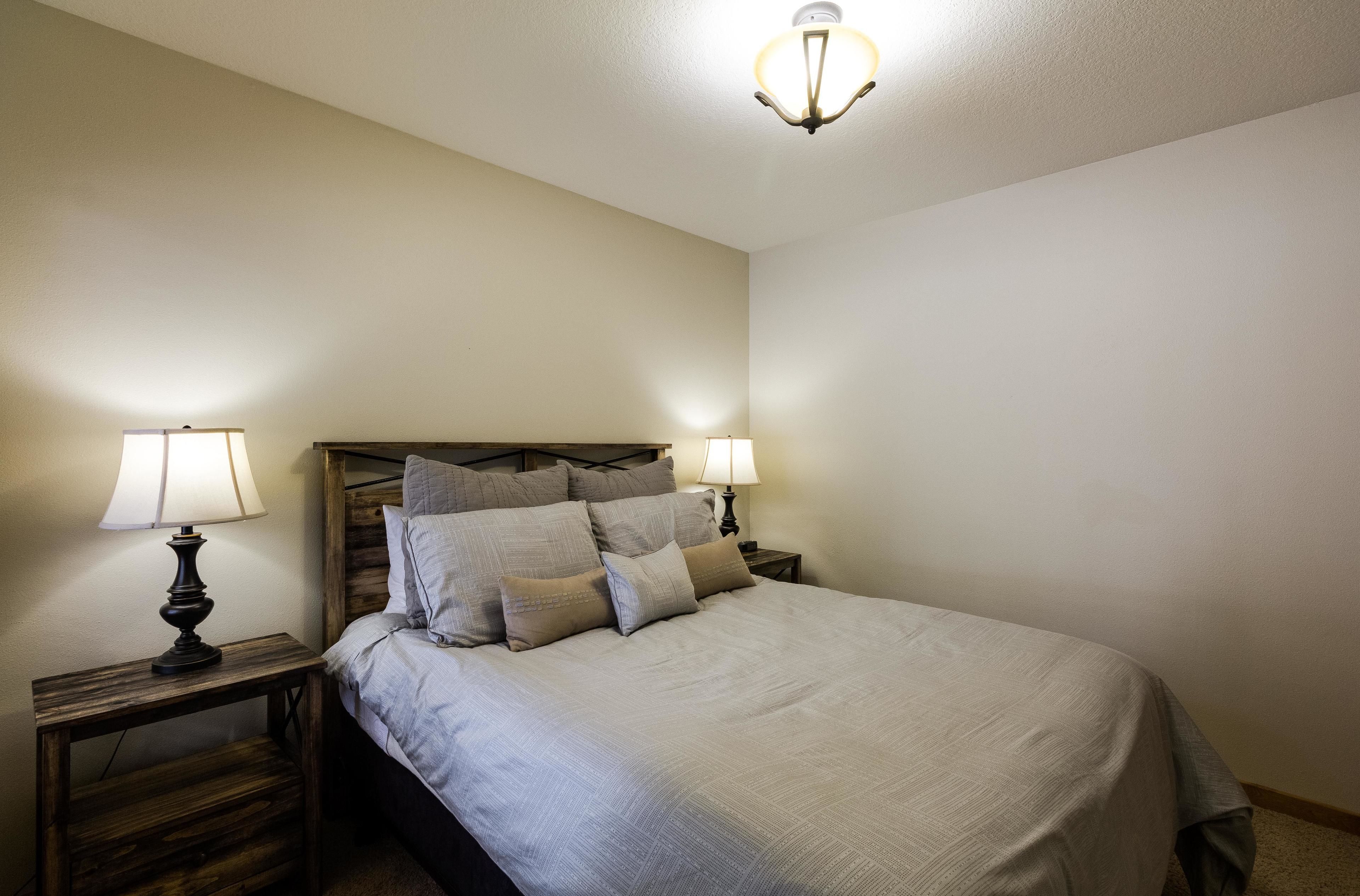 A bedroom with a bed, two bedside tables with lamps, and a ceiling light fixture.