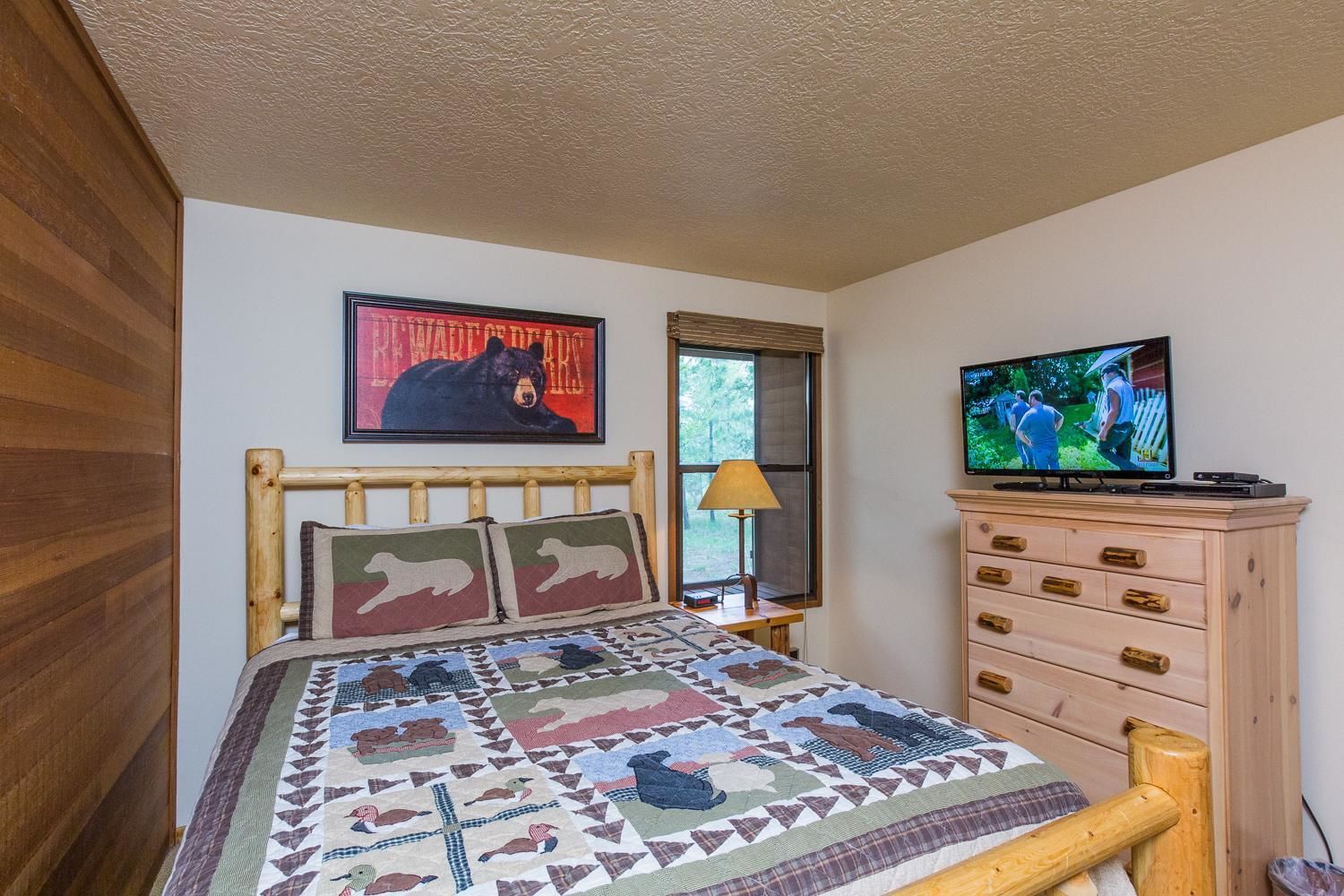 Ein Schlafzimmer mit einem hölzernen Bett, einer Steude mit Tiermotiven, einem Fernseher auf einer Kommode und einem Bärenbild an der Wand.