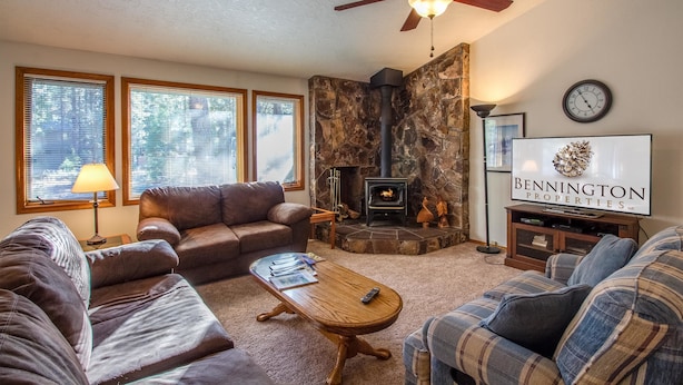 A cozy living room with a stone fireplace, a ceiling fan, and a television displaying 'Bennington Properties'.