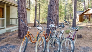 Bicycles parked against trees in a forested area with a house in the background.