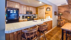 A kitchen with wooden cabinets, a black refrigerator, a microwave, and a stove. There are two wooden bar stools and a table with chairs. - Leisure 5 (Bend)