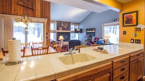 A kitchen with a large sink, wooden cabinets, and a dining area with chairs. - Leisure 5 (Bend)