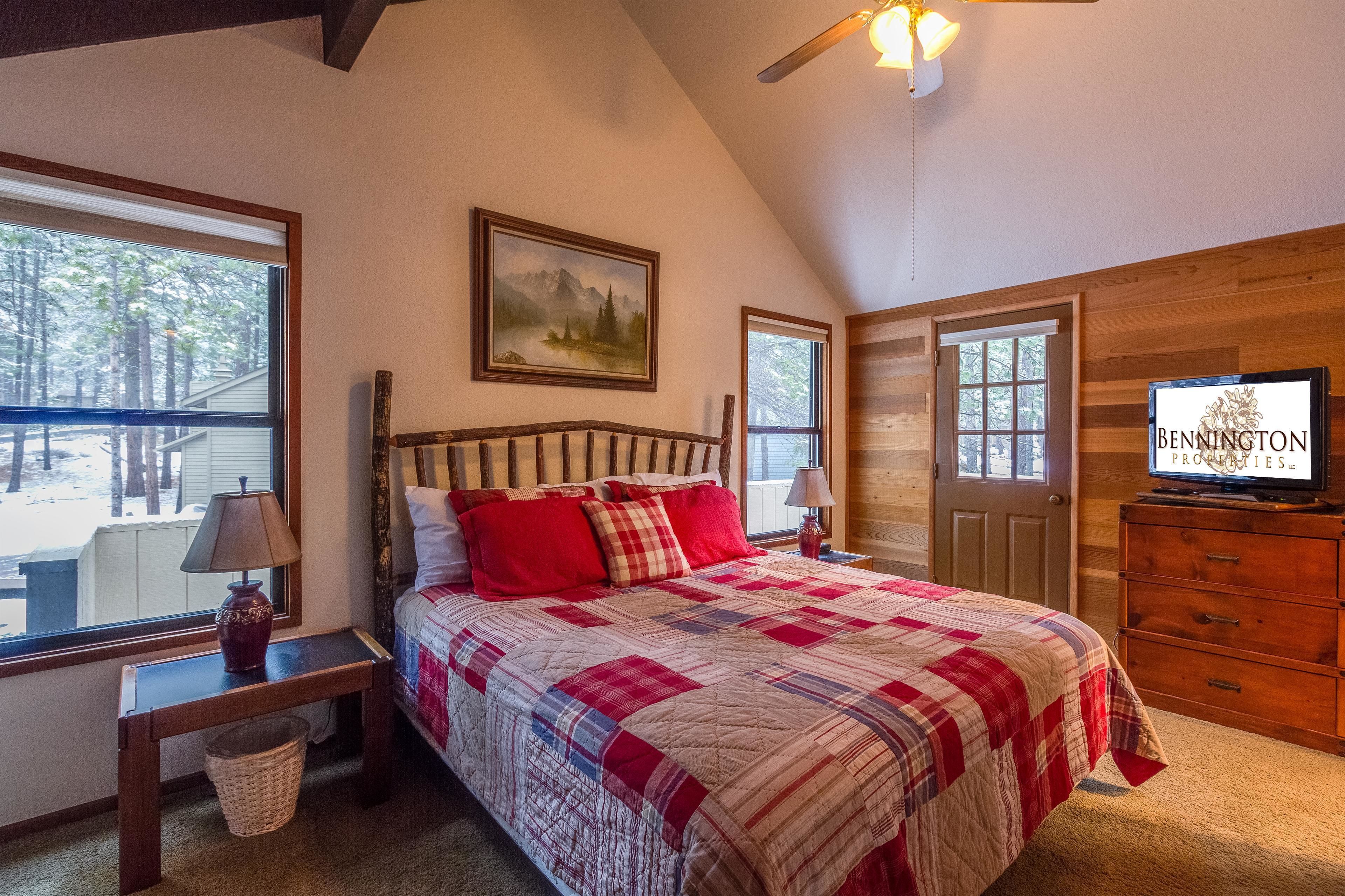 A bedroom with a large bed, a television, and a window with a view of trees.