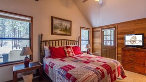 A bedroom with a large bed, a television, and a window with a view of trees. - Leisure 4 (Bend)