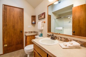 Ein Badezimmer mit Holztür, Toilette, Waschbecken mit Spiegel darüber und Handtuchhalter mit Handtüchern.