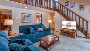 A spacious living room with a large blue sofa set, a wooden coffee table, and a staircase with wooden railings. - Leisure 4 (Bend)