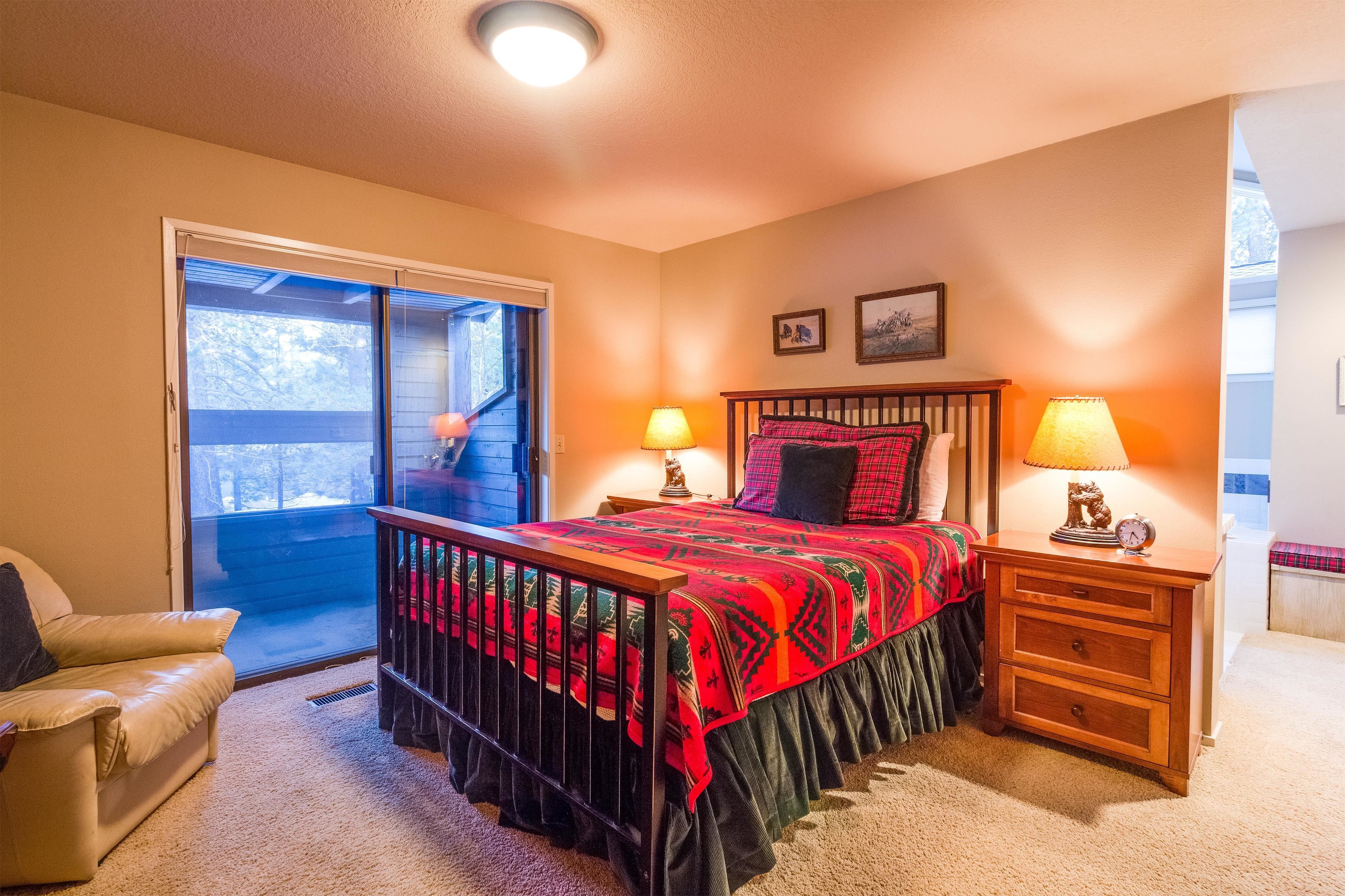 A bedroom with a bed, two nightstands, a chair, a window, and a door.
