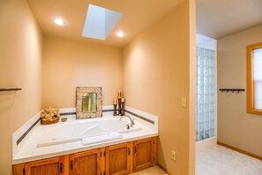 A bathroom with a large bathtub, wooden cabinets, a mirror, and a window with frosted glass. - Loon 6 (Bend)