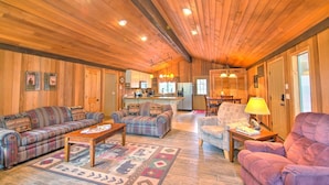 A cozy cabin interior with wooden walls and ceiling, a central living area with sofas and a coffee table, a kitchen with a refrigerator and sink, and a dining area with a table and chairs. - Lynx 5 (Bend)
