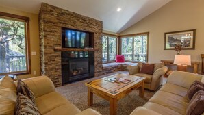 A cozy living room with a stone fireplace, comfortable leather sofas, a coffee table, and large windows offering a view of the outdoors. - Malheur 5 (Bend)