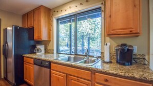 A kitchen with wooden cabinets, a stainless steel refrigerator, a dishwasher, a double sink, and a coffee maker. - Sparks 5 (Bend)