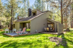 A cabin with a deck, outdoor seating, and a stone chimney. - Meadow Hse Cndo 5 (Bend)