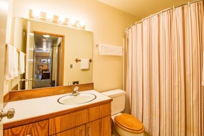 A bathroom with a wooden vanity, a sink, a mirror, and a striped shower curtain. - Meadow Hse Cndo 5 (Bend)
