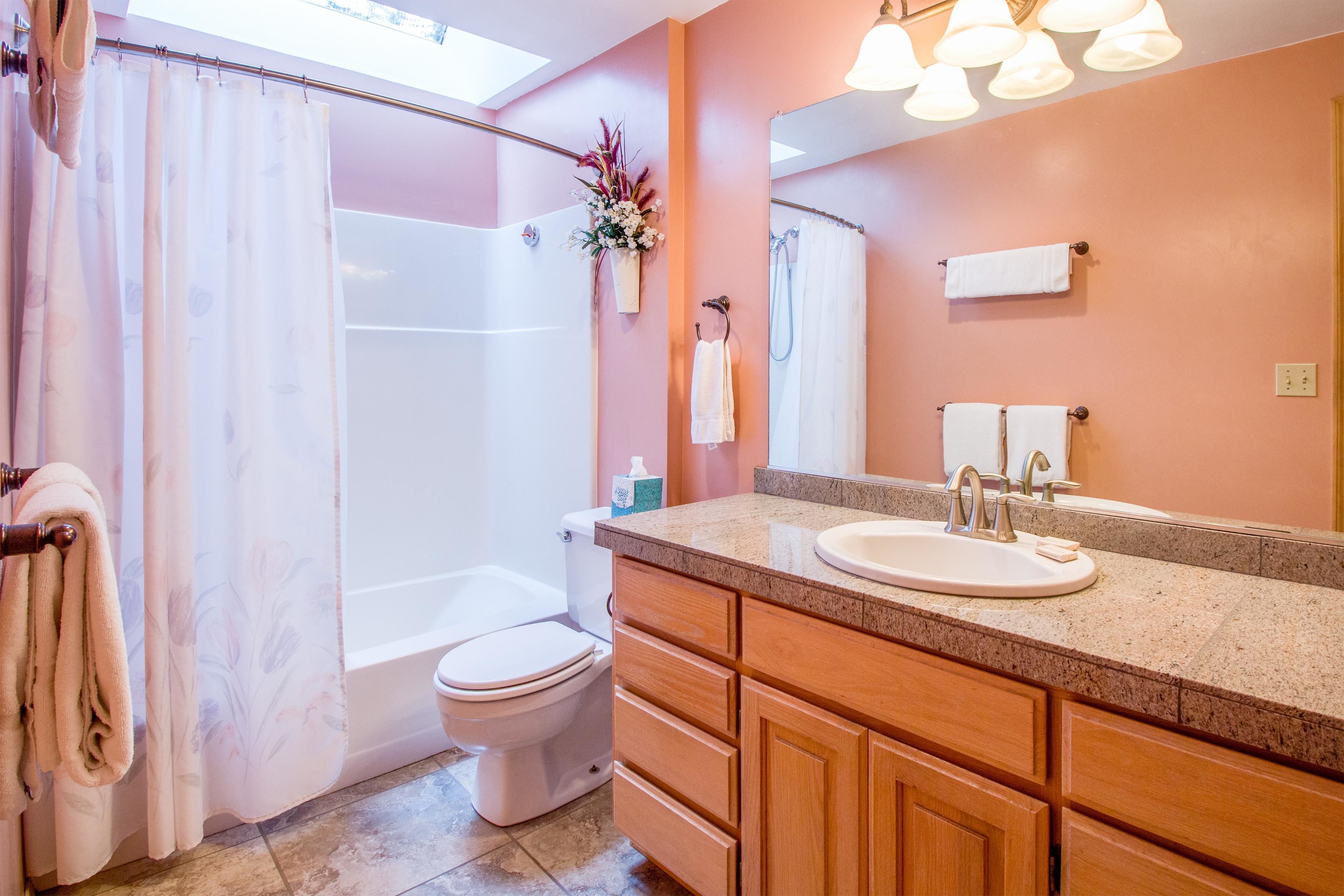 A bathroom with a shower, toilet, sink, and wooden cabinets.