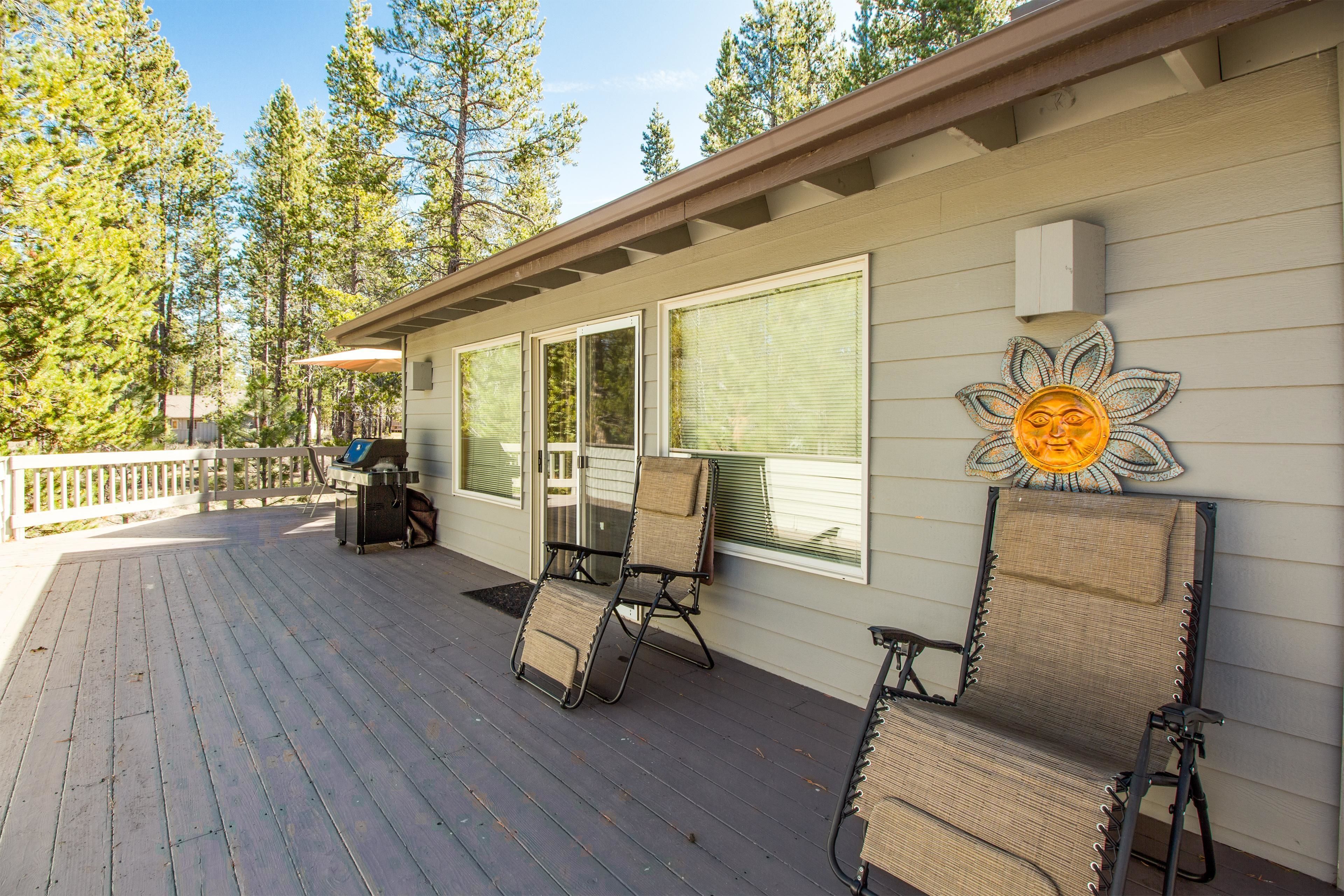 A covered deck with two lounge chairs and a table, overlooking a forested area.