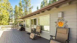 A covered deck with two lounge chairs and a table, overlooking a forested area. - Mt Rose 2 (Bend)