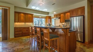 A spacious kitchen with wooden cabinets, a stainless steel refrigerator, and a bar area with stools. - Mt Rose 9 (Bend)