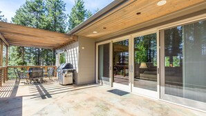 A covered patio area with a grill, outdoor furniture, and a sliding glass door leading to an outdoor seating area. - Mt Rose 9 (Bend)