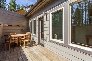 A wooden deck with a table and chairs, large windows, and a door.