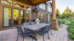 Une terrasse avec une grande table et des chaises, un barbecue et un mur en pierre.