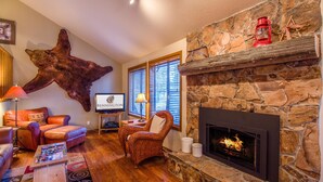 A cozy living room with a stone fireplace, leather furniture, and a mounted animal head. - Nine Iron 10 (Bend)