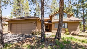A two-story house with a garage, surrounded by trees and a grassy yard. - Nine Iron 10 (Bend)