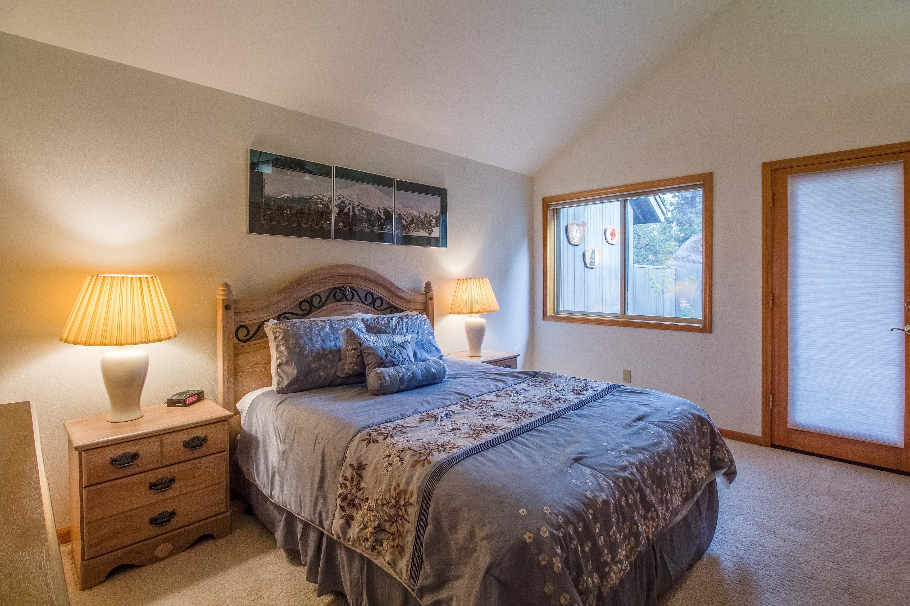 Une chambre à coucher comprenant un lit, deux tables de chevet avec des lampes, une commode, une fenêtre avec des stores et une porte.