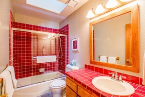 A bathroom with a red-tiled shower, a white bathtub, a white toilet, and a sink with a mirror above it. - Nine Iron 7 (Bend)