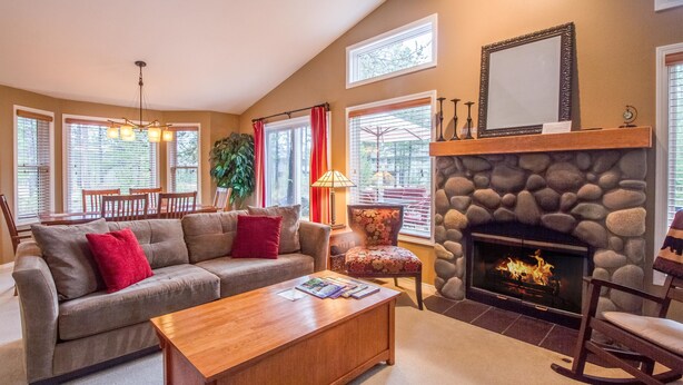 A cozy living room with a stone fireplace, a sofa, a coffee table, and a dining area with chairs and a table.