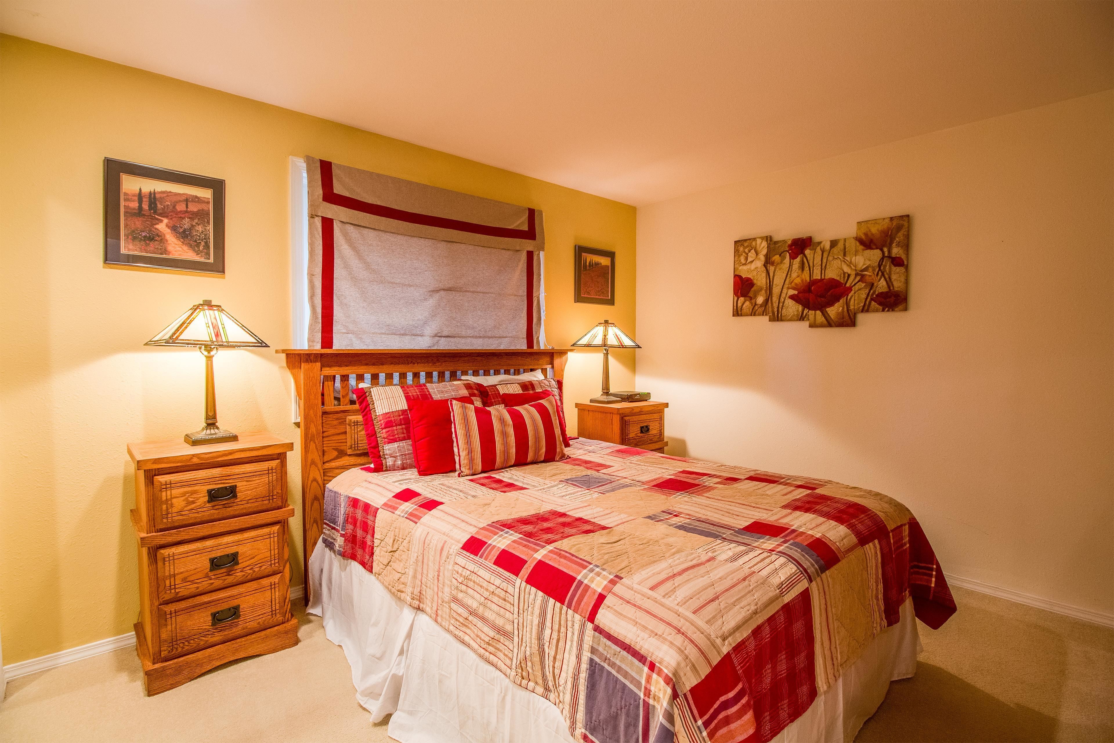 Quarto com cama de madeira, duas mesinhas de cabeceira, um criado-mudo e uma parede com obras de arte emolduradas.