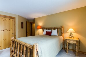A bedroom with a wooden bed frame, a bedside table with a lamp, and a door.